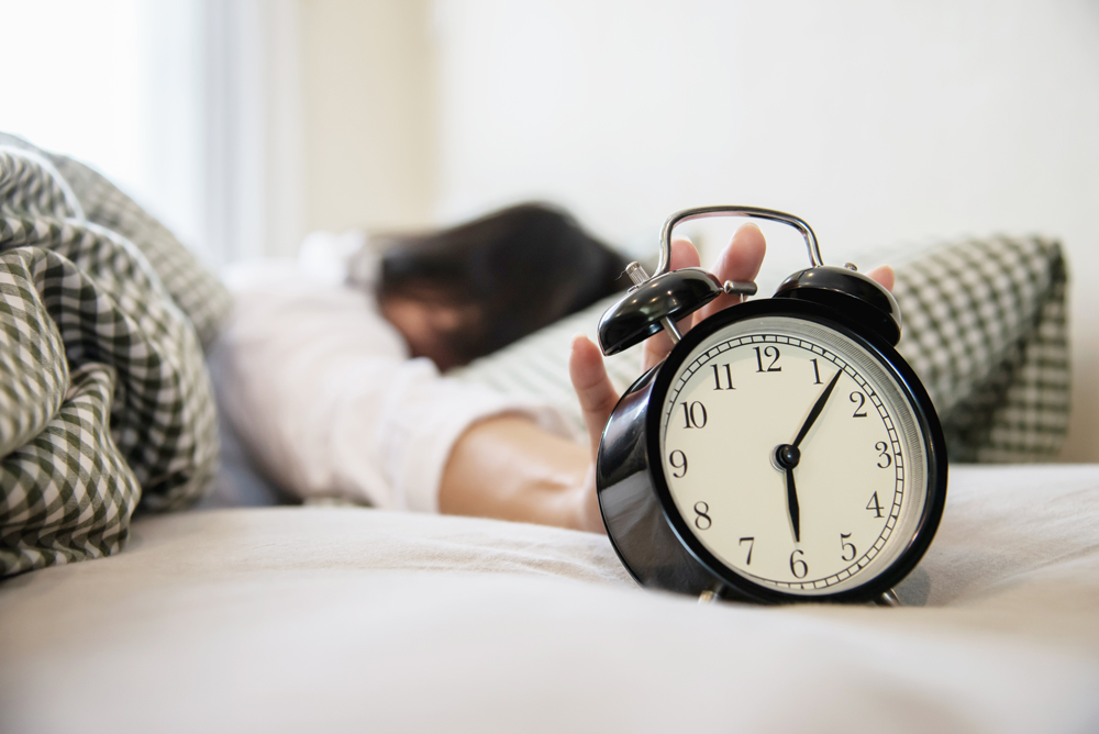 sleepy-woman-reaching-holding-the-alarm-clock